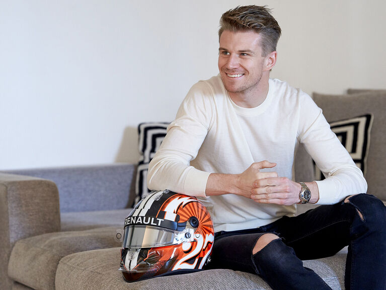 Nico Hülkenberg sitzt lächelnd und sich auf einem Formel-1-Helm abstützend auf einer Couch