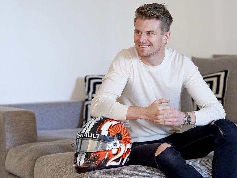 Nico Hülkenberg sitzt lächelnd und sich auf einem Formel-1-Helm abstützend auf einer Couch Nico Hülkenberg sitzt lächelnd und sich auf einem Formel-1-Helm abstützend auf einer Couch