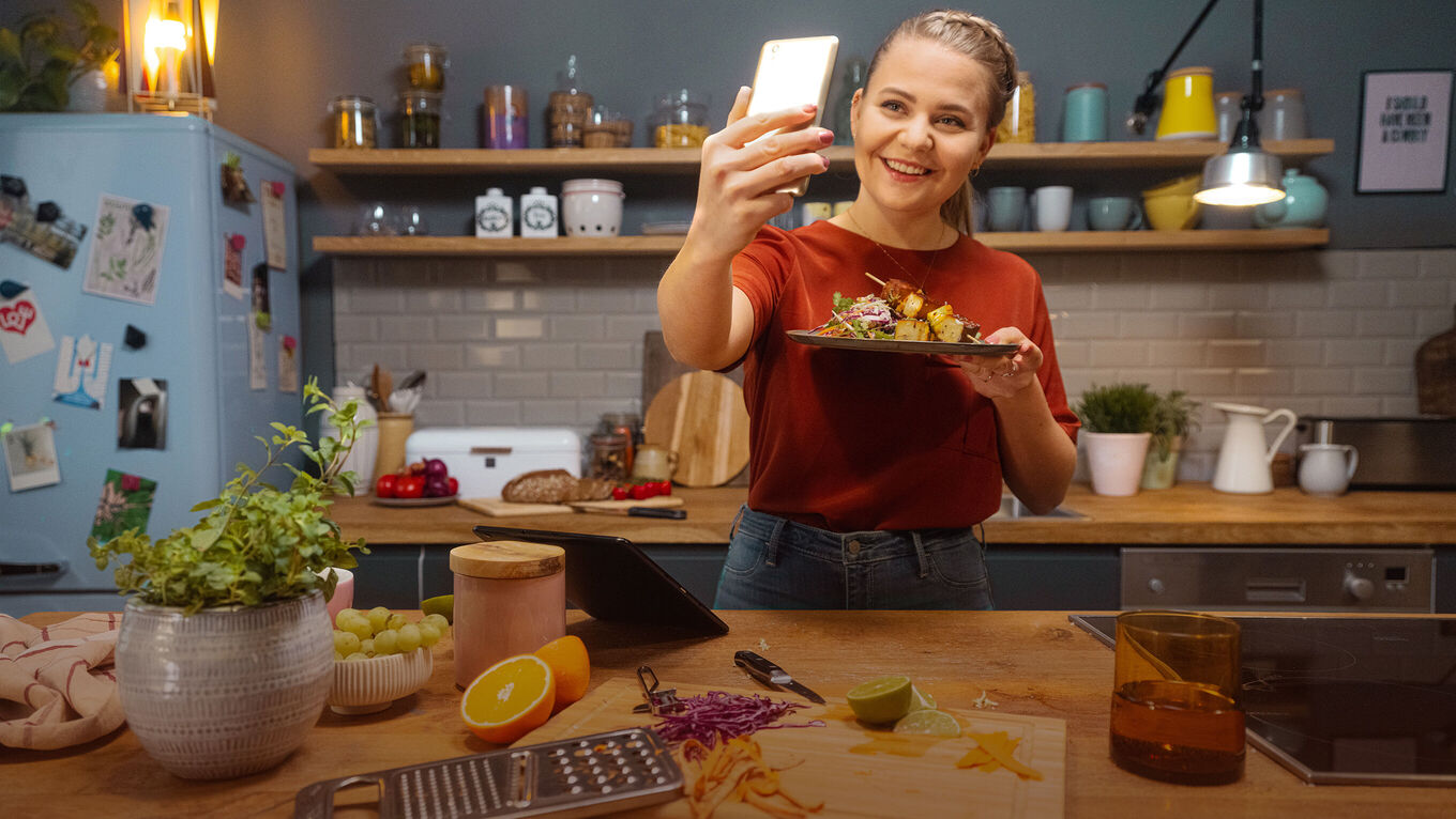Kati macht in atmosphärischer Küchenumgebung ein Selfie mit ihrem Teller in der Hand