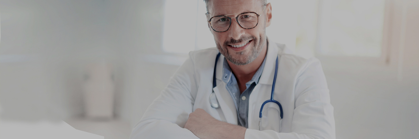 Sympathischer, männlicher Arzt im mittleren Alter, mit Brille, weißem Kittel und Stethoskop um den Hals, lächelt mit verschränkten Armen und direktem Blick