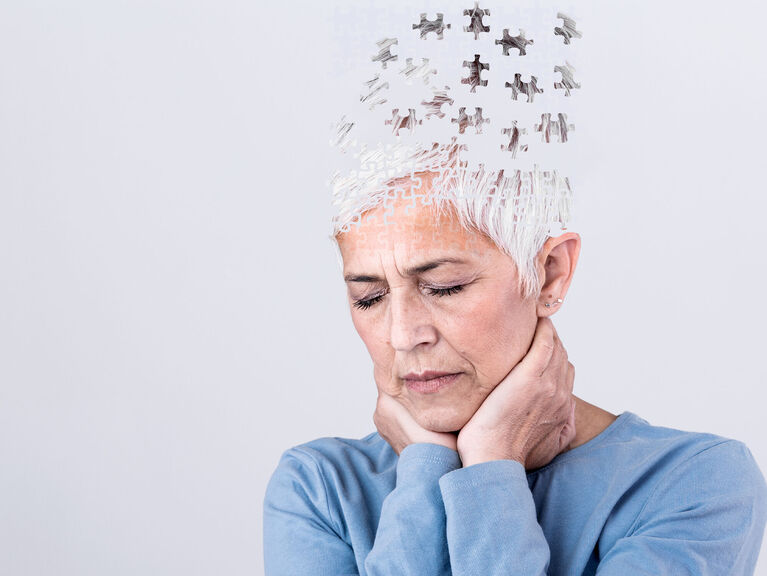 Fotomontage: Seniorin hält sich das Kinn, während, Teile ihres Kopfes als Puzzleteile davon fliegen