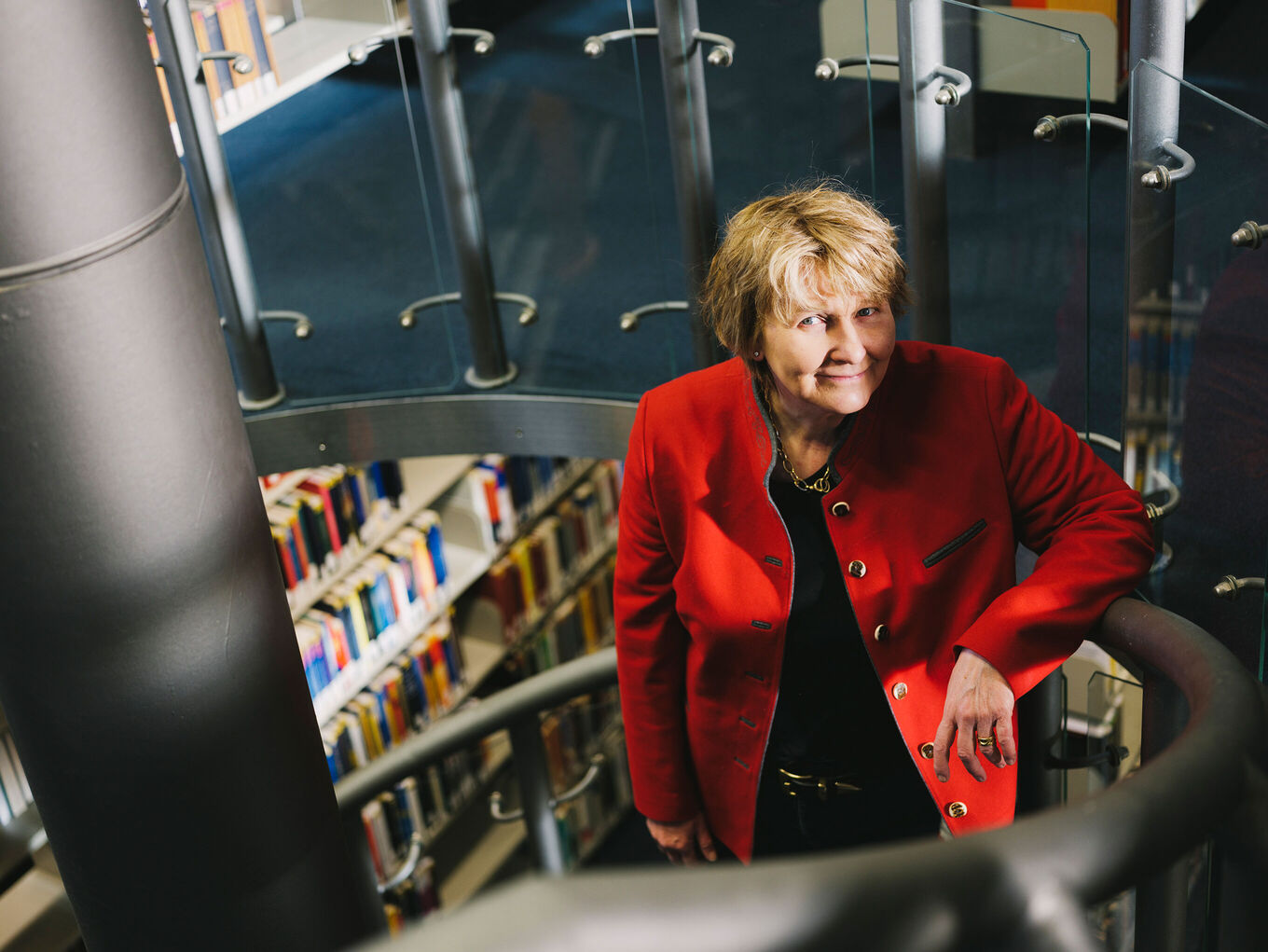 Michaela Brohm-Badry steht - mit Buchregalen im Hintergrund - auf der Treppe einer Bibliothek und lächelt freundlich