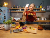 Kati macht in atmosphärischer Küchenumgebung ein Selfie mit ihrem Teller in der Hand