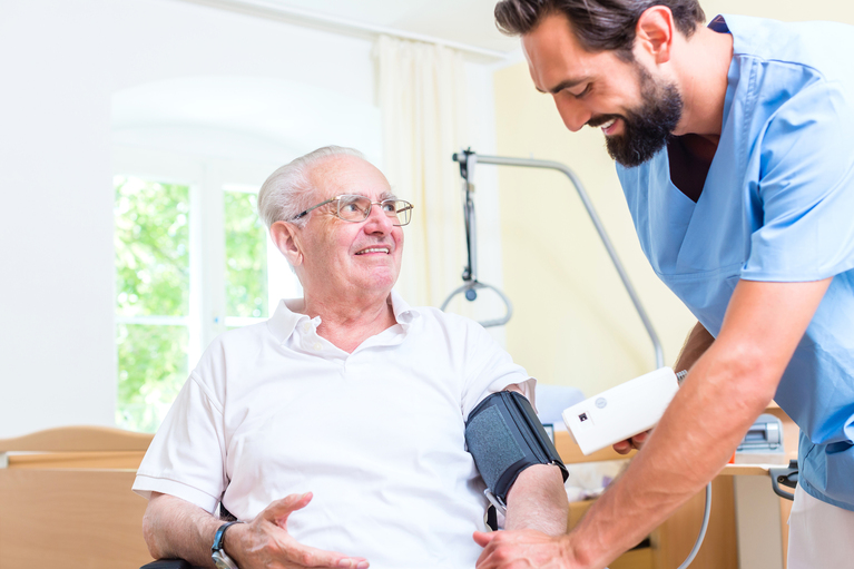 Lächelnder Pfleger legt fröhlichem Senior ein Blutdruckmessgerät an