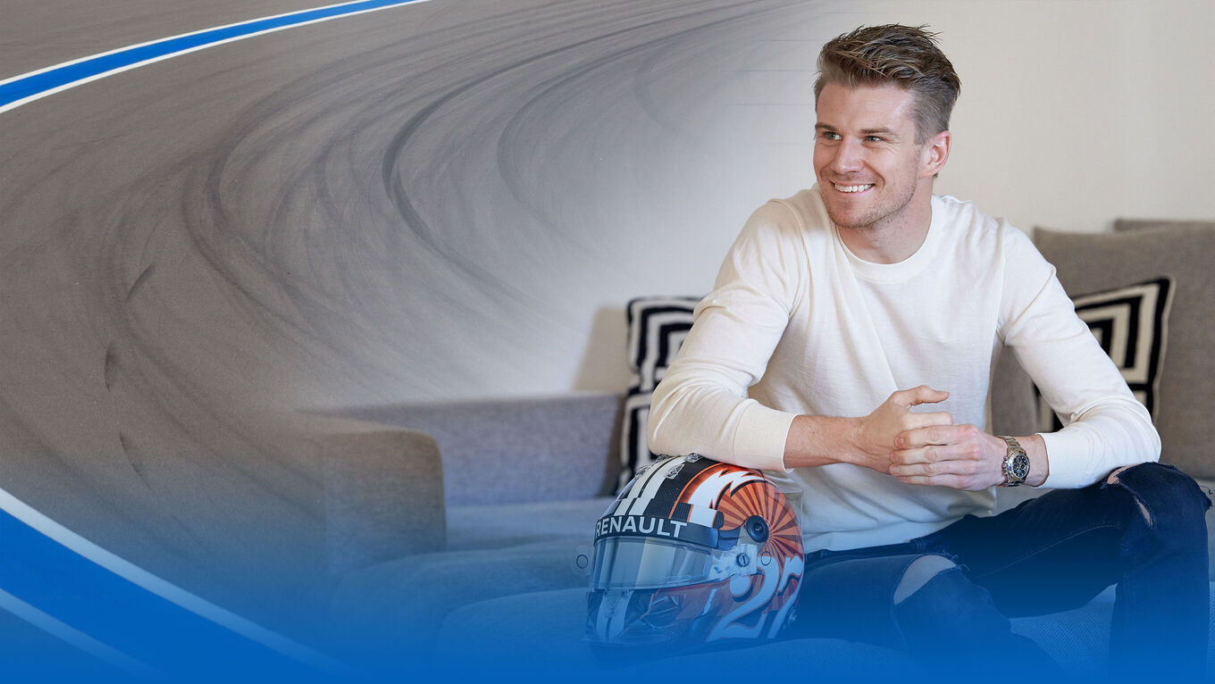 Nico Hülkenberg sitzt lächelnd und sich auf einem Formel-1-Helm abstützend auf einer Couch