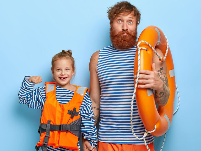 Lächelnder Mann im Retro-Badeanzug mit Rettungsring, lächelndes Kind mit Schwimmweste Lächelnder Mann im Retro-Badeanzug mit Rettungsring, lächelndes Kind mit Schwimmweste