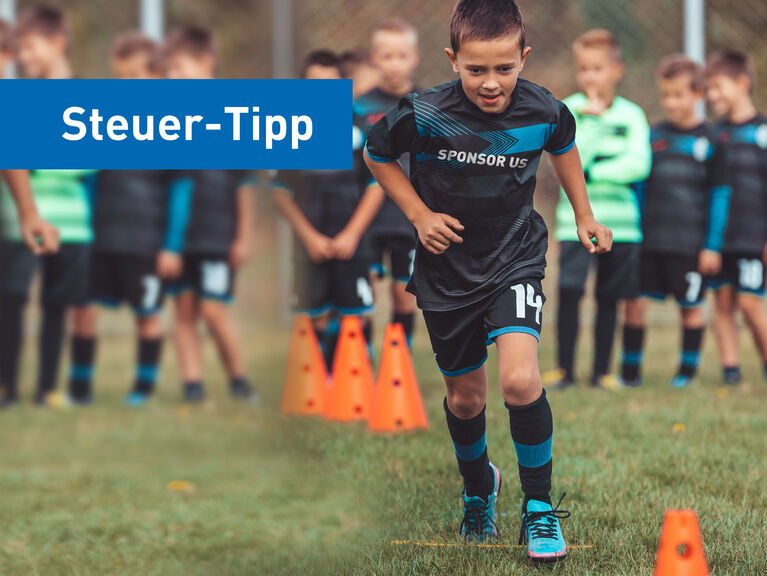 Gruppe von Grundschuljungs macht Lauftraining auf Rasenfußbalplatz, ein Junge im Fokus hat den Schriftzug "sponsor us" auf dem Trikot Gruppe von Grundschuljungs macht Lauftraining auf Rasenfußbalplatz, ein Junge im Fokus hat den Schriftzug "sponsor us" auf dem Trikot
