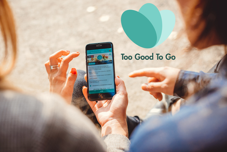 Zwei Personen in Rückenansicht betrachten Smartphone mit Screen der App "Too good to go"