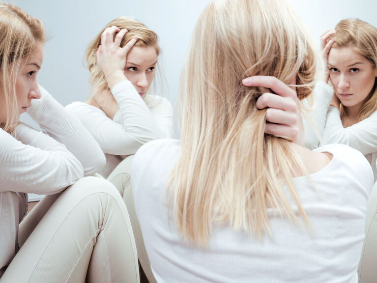 Junge Frau in Rückenansicht schaut sich selbst, wie in einem Spiegelkabinett, vierfach ins Gesicht. Sie scheint verwirrt und traurig Junge Frau in Rückenansicht schaut sich selbst, wie in einem Spiegelkabinett, vierfach ins Gesicht. Sie scheint verwirrt und traurig