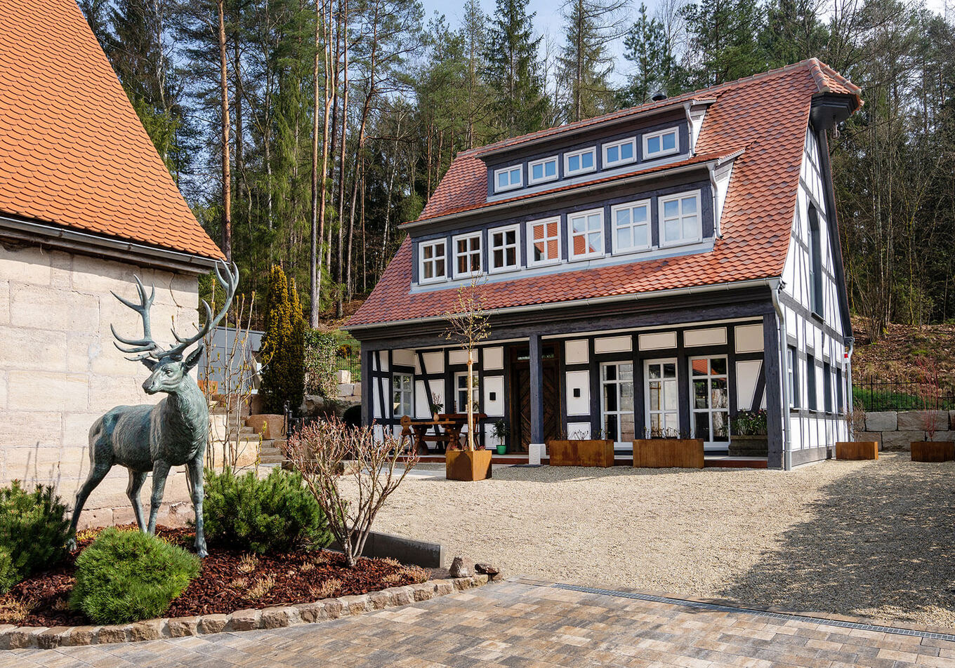 Idyllische Ansicht eines freistehenden Fachwerkhauses inklusive Vorhof und Wald im Hintergrund