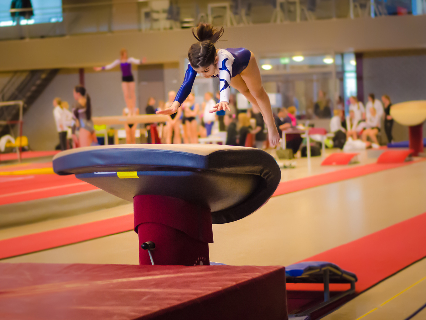 Mädchen in Turnanzug springt in einer Turnhalle über einen Turnbock