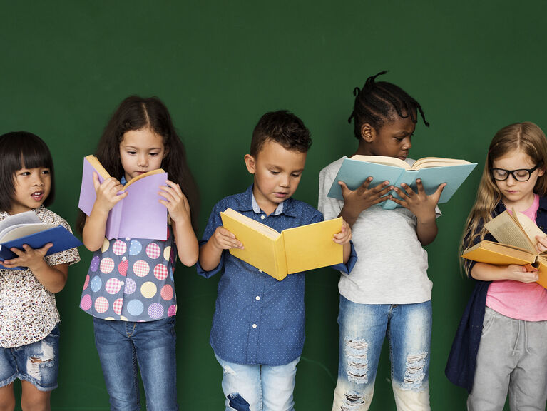 Fünf ethnisch diverse Kinder stehen nebeneinander lesend vor einer dunkelgrünen Tafel Fünf ethnisch diverse Kinder stehen nebeneinander lesend vor einer dunkelgrünen Tafel