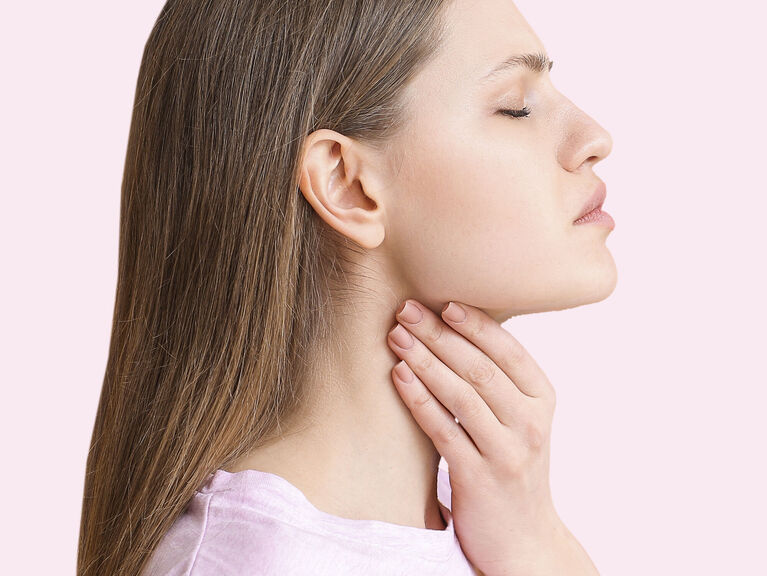 Junge Frau im Profil vor rosafarbenem Hintergrund fast sich mit geschlossenen Augen an den Hals
