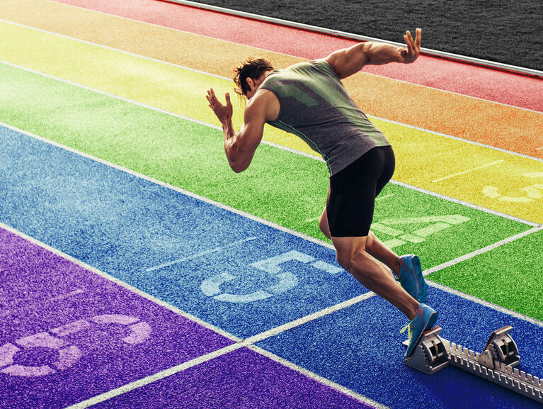 Läufer startet seinen Sprint von einem Startblock auf einer regenbogenfarbenen Tartanbahn