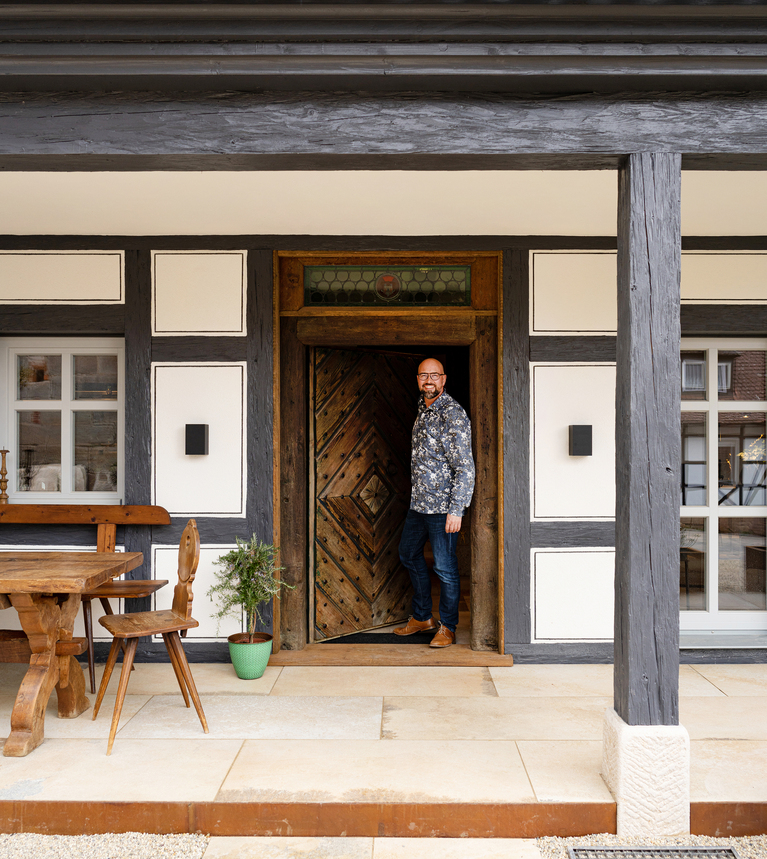 Sven Bartosch steht in der offenen Tür eines Fachwerkhauses mit großer, überdachter Terrasse
