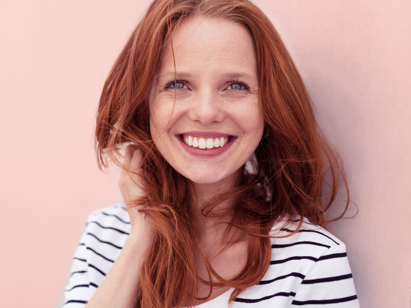 Portrait einer lachenden junge Frau in hellem Oberteil vor pastellrosafarbenem Hintergrund
