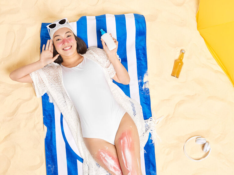 Mit Sonnencreme eingecremte Frau liegt auf Badetuch im Sand Mit Sonnencreme eingecremte Frau liegt auf Badetuch im Sand