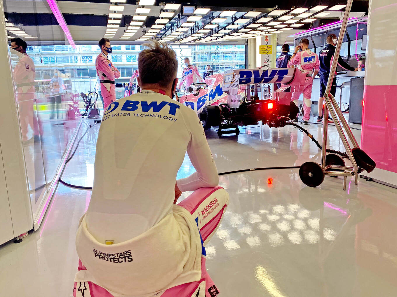 Niko Hülkenberg hockt in Rückenansicht mit Blick auf seinen Formel-1-Wagen und sein Team in der Garage des Rennstalls