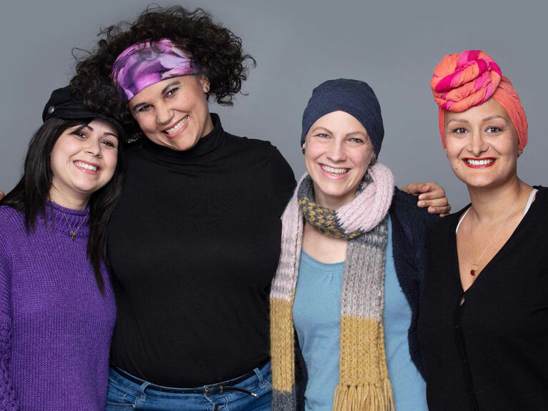 Vier lächelnde Krebspatientinnen, teils mit Kopfbedeckung